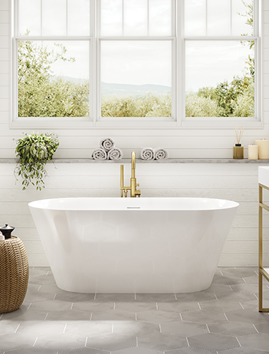 La baignoire autoportante en acrylique blanc Cadenza Petite de Fleurco dans une salle de bain lumineuse. Il y a une grande fenêtre derrière la baignoire et tous les murs sont blancs.