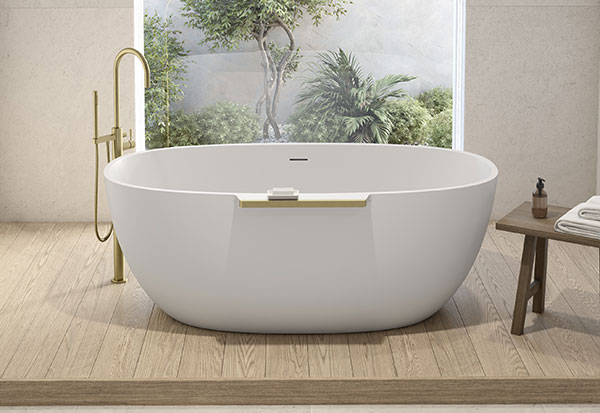 Une baignoire blanche avec des touches d'or brossé au centre d'une salle de bains qui révèle la beauté de la nature