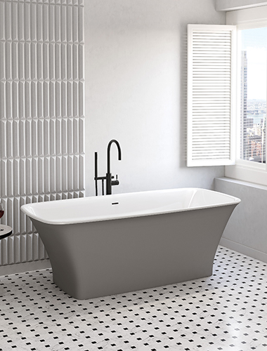 Baignoire en surface solide Lys de Fleurco. L'intérieur est blanc brillant et l'extérieur gris pierre foncé mat. La baignoire présente une forme rectangulaire symétrique, mais s'évase subtilement à son extrémité. Elle se trouve dans une pièce moderne aux tons gris, avec un sol à carreaux noirs et blancs et des murs gris. Une fenêtre ouverte se trouve dans un coin.