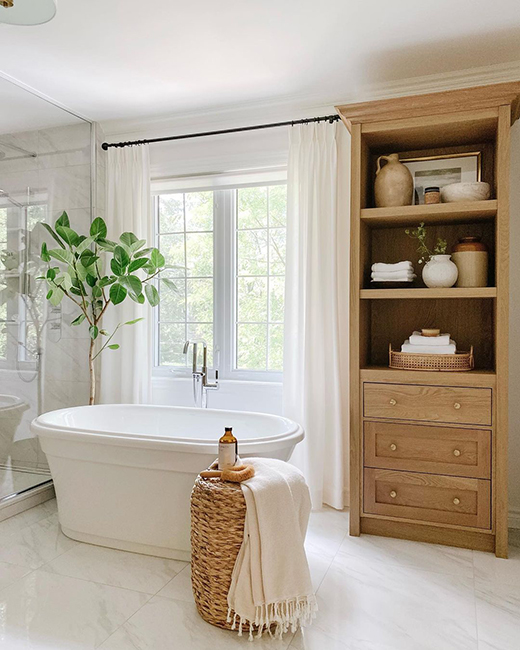 une baignoire en acrylique blanc brillant dans une salle de bain blanche avec une armoire en bois et un panier tressé