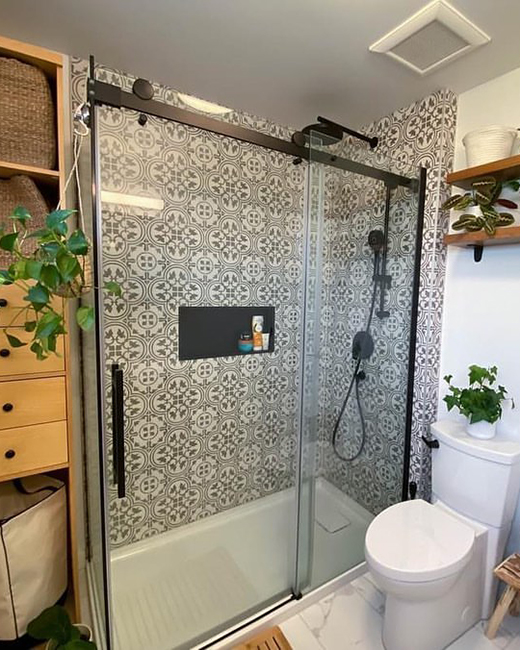 une porte de douche noire mate, avec des carreaux de douche à motifs noirs et blancs audacieux. la salle de bain est décorée de plusieurs plantes