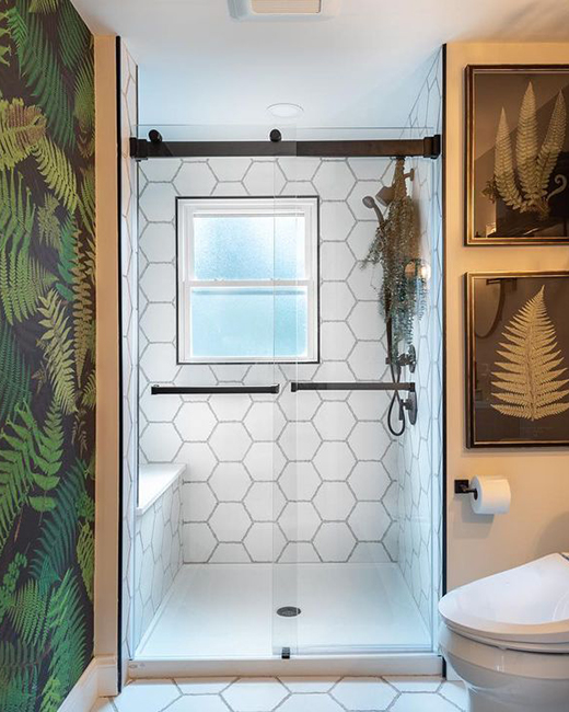 a matte black shower door in a white shower enclosure. bathroom has a large accent wall with leafy textures and is decorated with leafy artwork